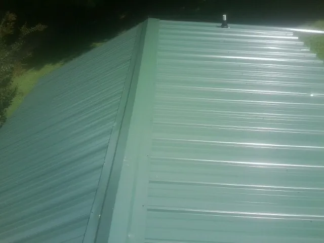New green metal panels meeting at the ridge of a roof — Flat Roof Repair work by our crew in Egg Harbor