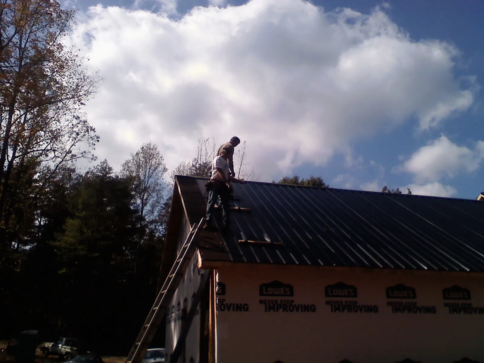 Roofer fastening dark metal panels high against a cloudy sky, from a Roof Inspection job in Egg Harbor