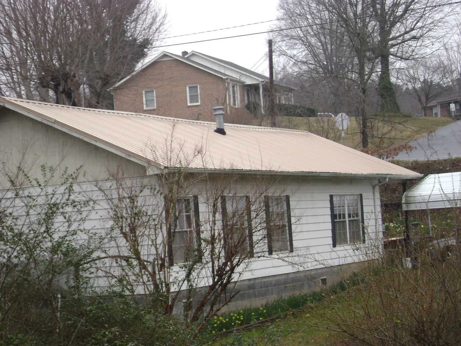 Tan metal roof on a white sided house set into a hillside — Commercial Roofing by Roofing Brothers in Egg Harbor